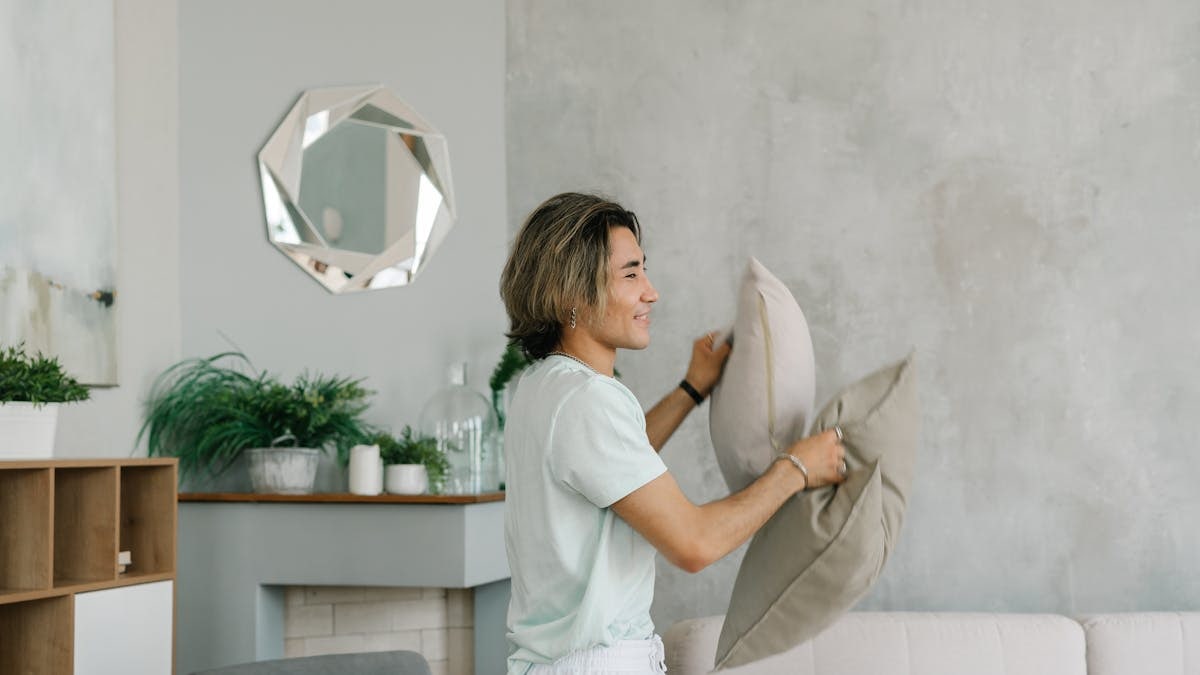 A young adult arranges pillows in a stylish, modern living room setting.