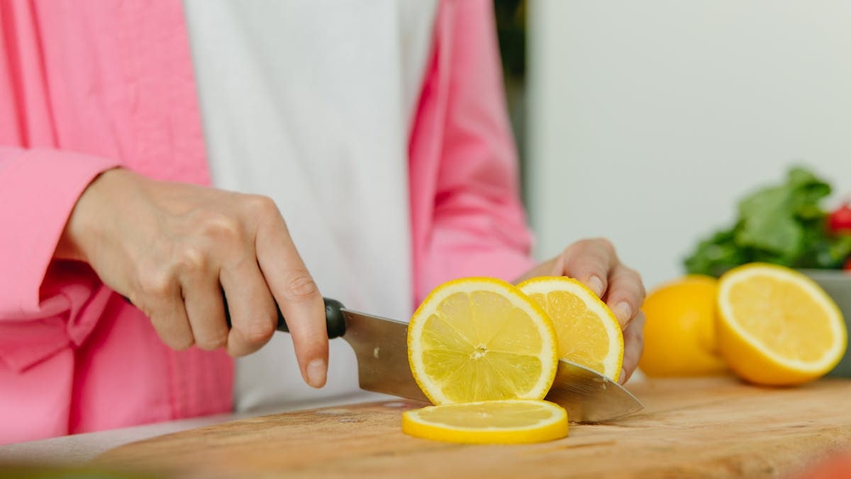 A close-up photo of hands slicing a lemon on a wooden chopping board, perfect for culinary or kitchen themes.